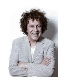Leo Sayer smiling with arms folded in a grey jacket