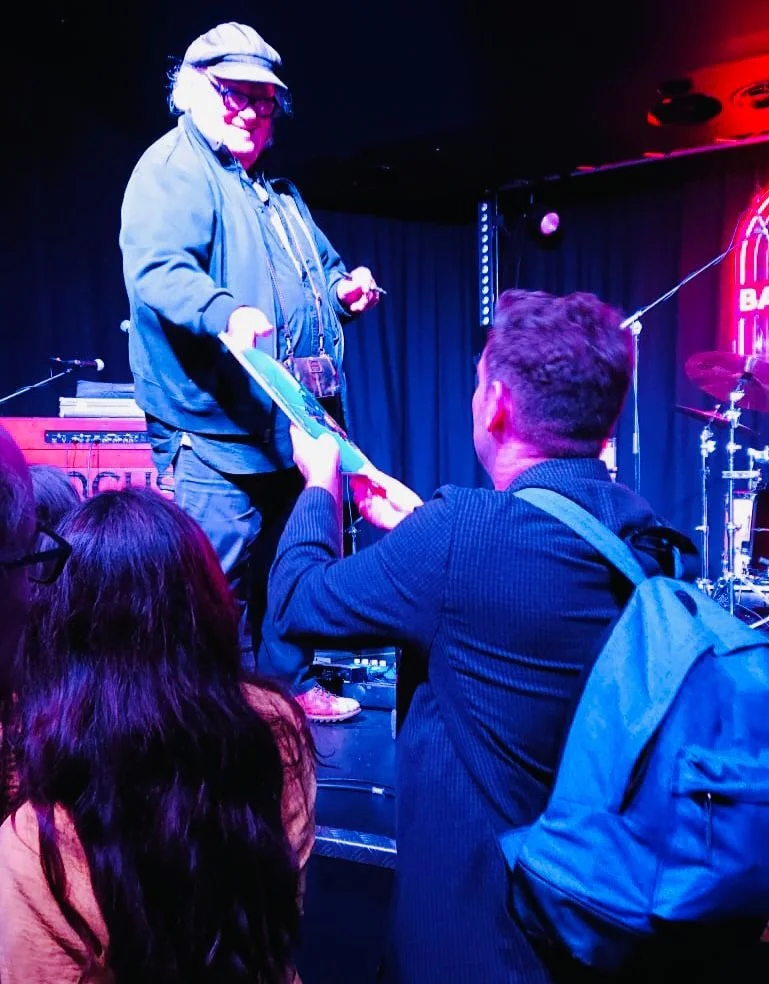 A musician in a cap reaches down from the stage to a fan at Band on the Wall