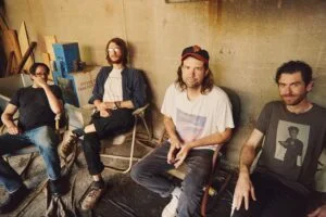 Wild Pink, four band members seated in a cluttered room, photo by Mitchell Wojcik