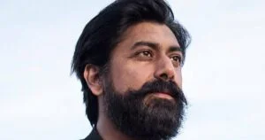 A bearded man in profile against a pale sky