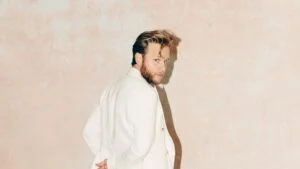 Olly Murs in a white jacket against a pale wall