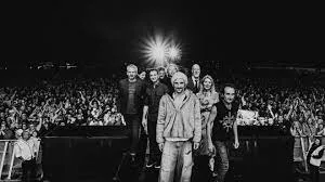 James, the band members, posing on stage before a large crowd, in black and white