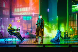 Actors on a neon-lit stage in Macbeth at Liverpool Playhouse