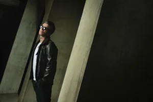 Noel Gallagher in a leather jacket against concrete pillars, photo by Matt Crockett