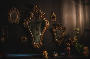 Ornate gilt mirrors on a dark wall with candles and a skull