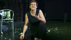 A performer in a black dress crouching on a dark stage