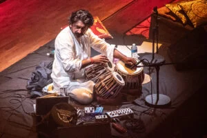 A tabla player in white performing with electronics on stage at the Tung Auditorium