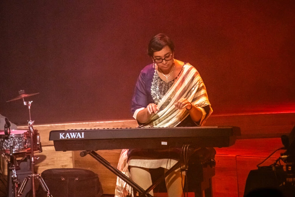 A keyboard player in a striped shawl performing at the Tung Auditorium
