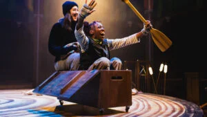 Two actors in a wooden boat, one raising an oar, in The Wind in the Willows at Shakespeare North Playhouse