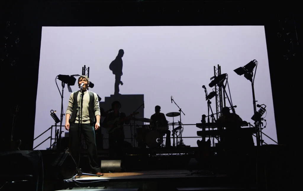 A singer on a stark white-lit stage in Come Together, photo by Andrew AB Photography