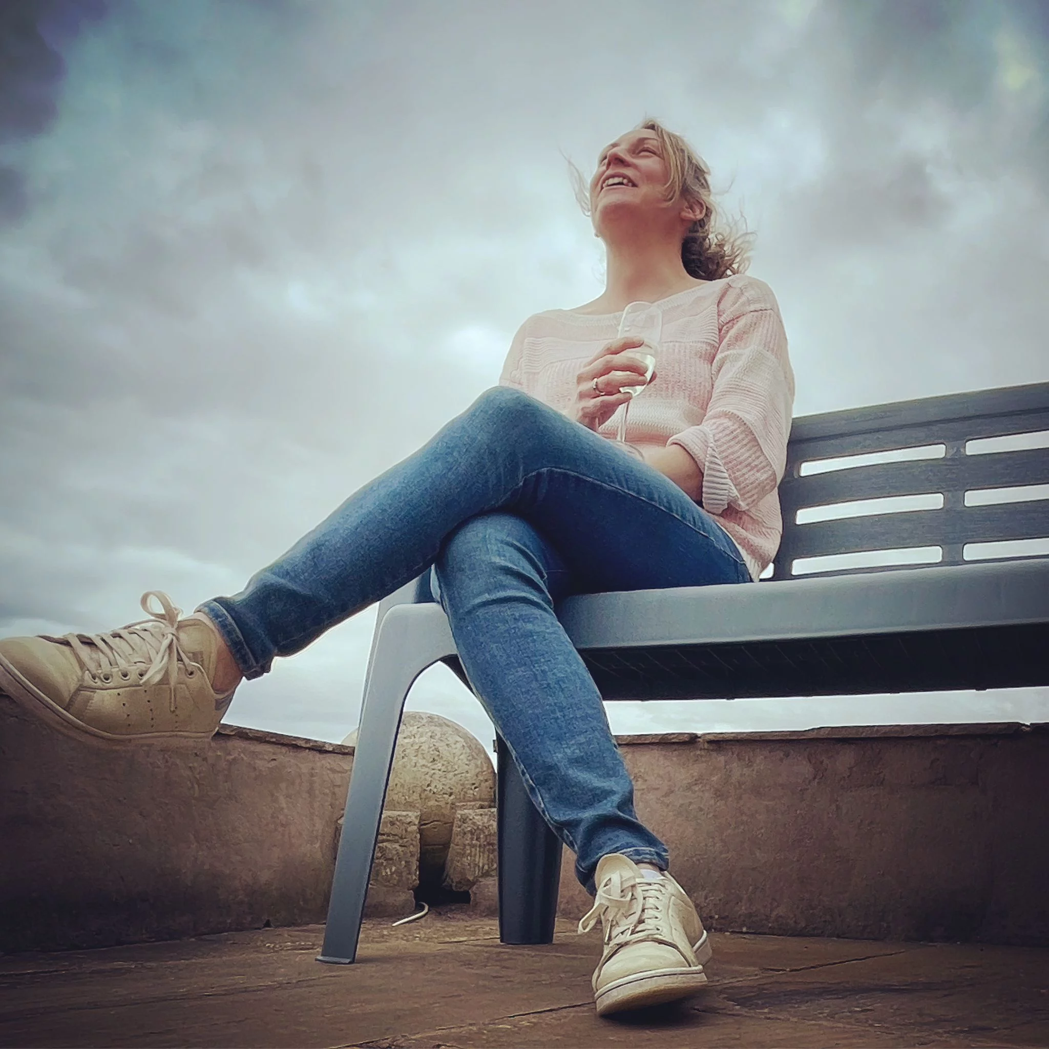 Katie Jenkins, Co-Poetry Editor at The Broken Spine, laughing on a bench under a cloudy sky