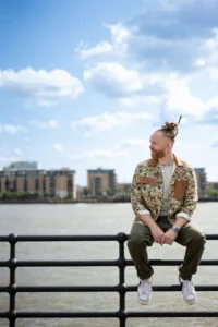 Newton Faulkner sitting on railings beside a river