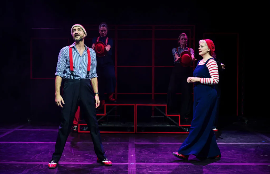 Showstoppers performers in braces and striped tops on a purple-lit stage, photo by Alex Brenner
