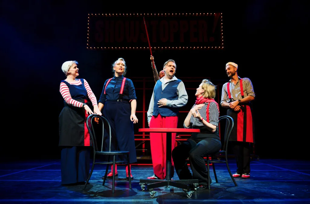 The Showstoppers cast on stage, one pointing upwards, photo by Alex Brenner
