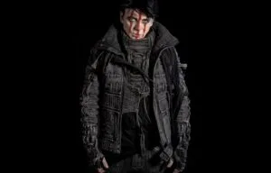 A figure in a dark hooded jacket against a black background