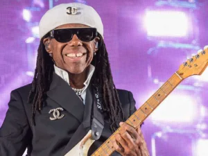 Nile Rodgers in a white cap and sunglasses playing guitar
