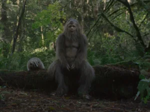 Still from Sasquatch Sunset: a Sasquatch sitting on a log in the forest