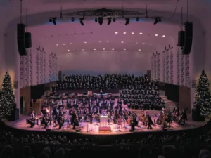 An orchestra and choir on stage at Liverpool Philharmonic Hall with Christmas trees