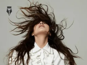 A woman in a white ruffled shirt with long dark hair flung across her face