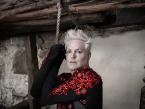 Andy Bell in a red embroidered jacket beside a rope