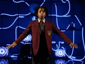 A young actor in a school blazer with arms outstretched in Pig Heart Boy