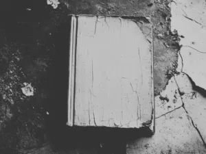 A worn book lying on a cracked stone floor, in black and white