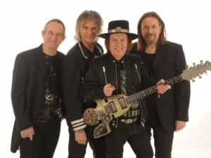 Slade, four band members dressed in black, one holding a guitar
