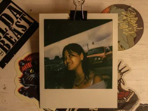 Polaroid of a smiling young woman clipped above a board covered in stickers