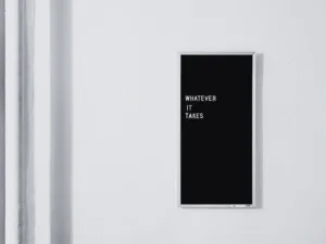 A black letter board on a white wall reading 'Whatever it takes'
