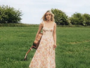 Rianne Downey in a floral dress holding a guitar in a field