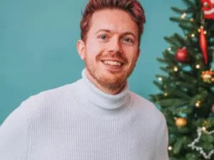 James B Partridge in a white roll-neck beside a Christmas tree