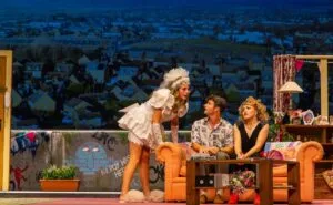 Three actors around an orange sofa on a rooftop set in The Peaceful Hour 2 at the Royal Court