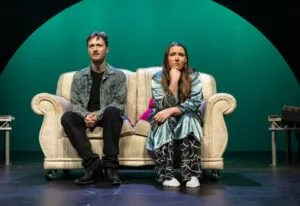 Two actors on a cream sofa in Under the Mersey Moon at the Floral Pavilion